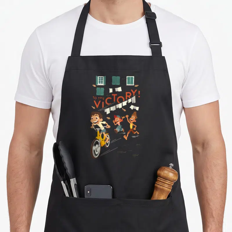 Tablier de cuisine noir avec illustration d'un vélo jaune, de personnages courant et du texte To The Victory au-dessus de rideaux blancs.
