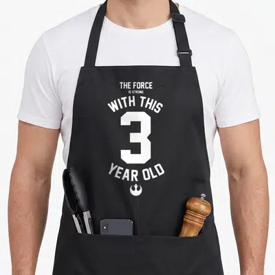 Tablier de cuisine noir avec inscription blanche The Force Is Strong With This 3 Year Old Rebel Logo et logo de la Rébellion en bas.