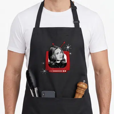Tablier de cuisine noir avec illustration télévision rouge vintage et portrait de femme aux cheveux foncés entouré d'étoiles blanches.