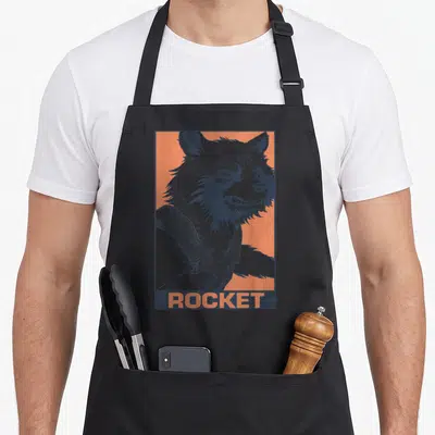 Tablier de cuisine noir avec illustration pop art du personnage Rocket sur fond orange et texte ROCKET en bas.