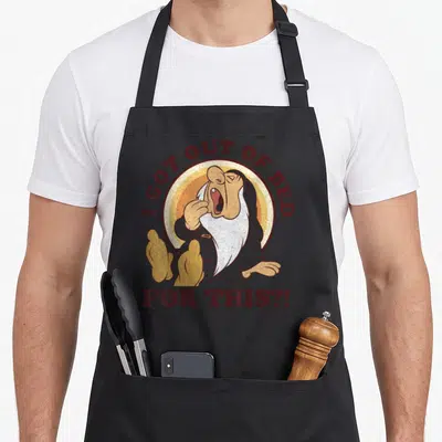 Tablier de cuisine noir avec un nain endormi et le texte I GOT OUT OF BED FOR THIS en lettres marron.