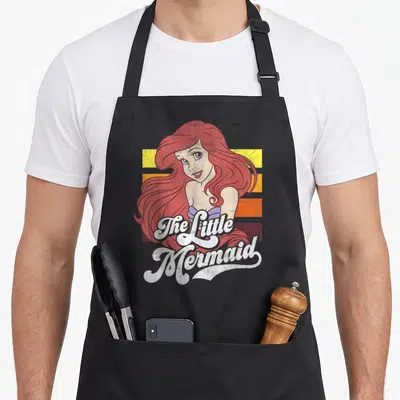 Tablier de cuisine noir avec illustration vintage de La Petite Sirène et texte The Little Mermaid sur bandes colorées.