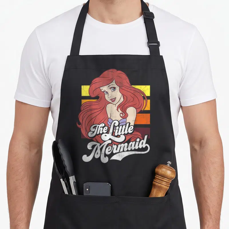 Tablier de cuisine noir avec illustration vintage de La Petite Sirène et texte The Little Mermaid sur bandes colorées.