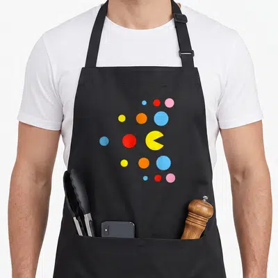Tablier de cuisine noir avec illustration géométrique colorée de Pac-Man et de points multicolores.