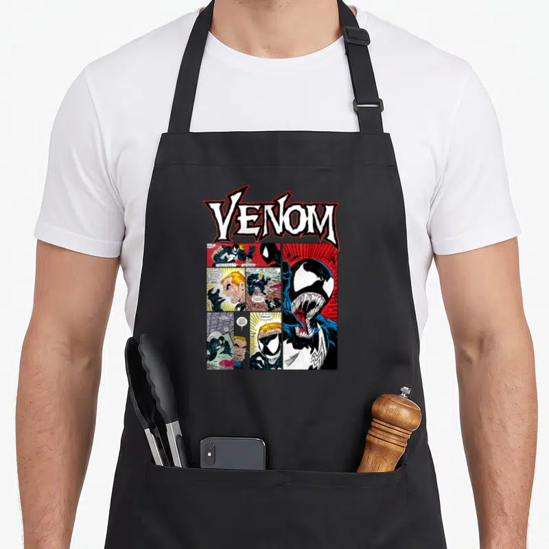 Tablier de cuisine noir avec le logo Venom et des vignettes de comics classiques imprimées au centre.