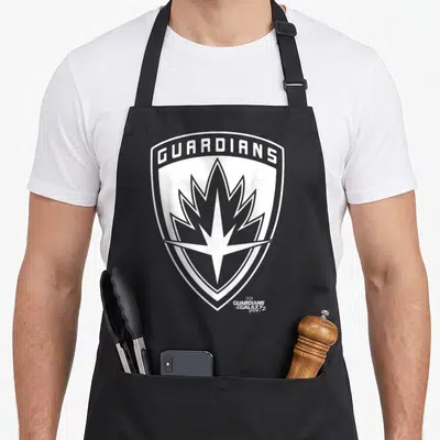 Tablier de cuisine noir avec un grand logo blanc en forme de bouclier portant le texte Guardians et une étoile stylisée au centre.