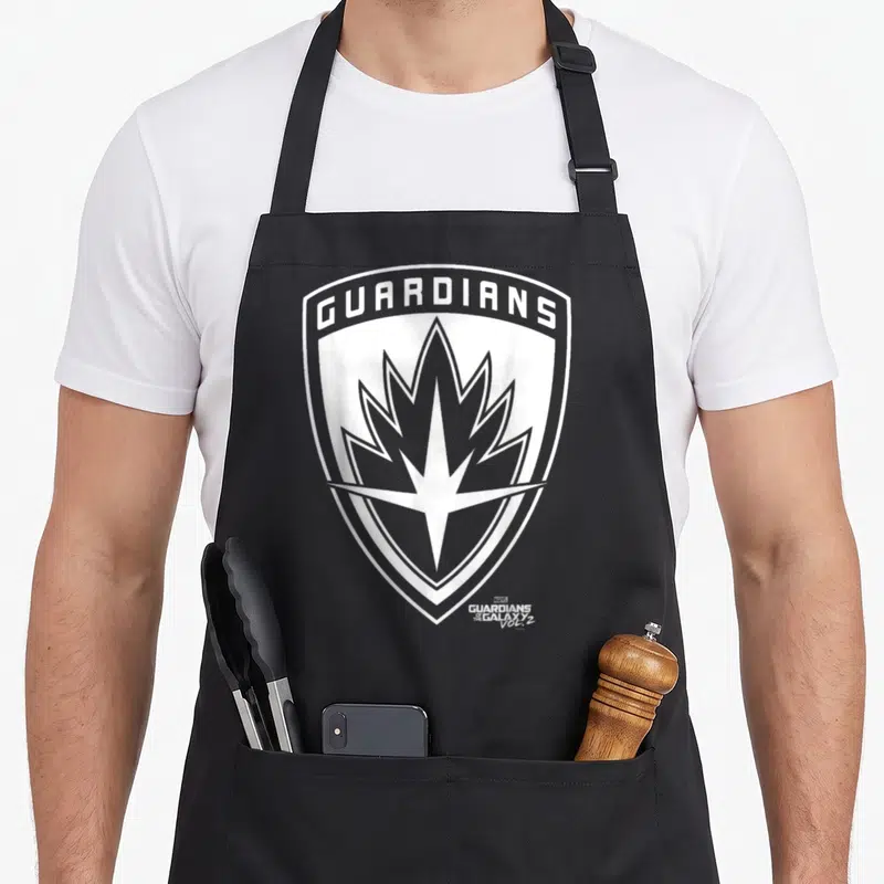 Tablier de cuisine noir avec un grand logo blanc en forme de bouclier portant le texte Guardians et une étoile stylisée au centre.