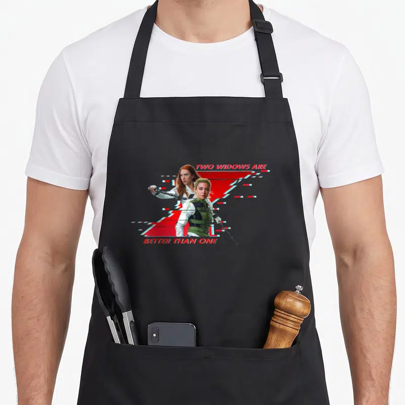 Tablier de cuisine noir avec deux héroïnes Marvel tenant des bâtons devant un logo rouge fragmenté.
