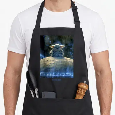 Tablier de cuisine noir avec Grogu assis sur une roche et le logo The Mandalorian en bas.