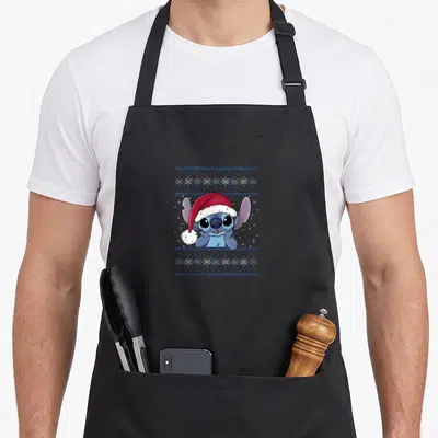 Tablier de cuisine noir avec Stitch en bonnet rouge entouré de motifs de flocons et de bandes décoratives bleues.