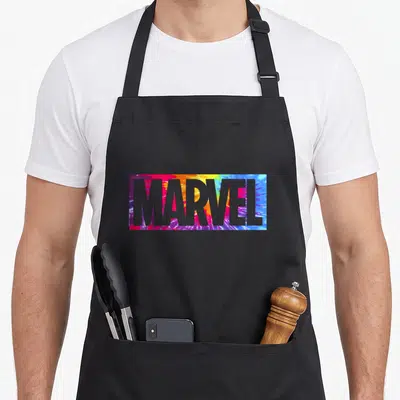 Tablier de cuisine noir avec un rectangle tie dye rose bleu vert portant le mot MARVEL en grosses lettres capitales grises.