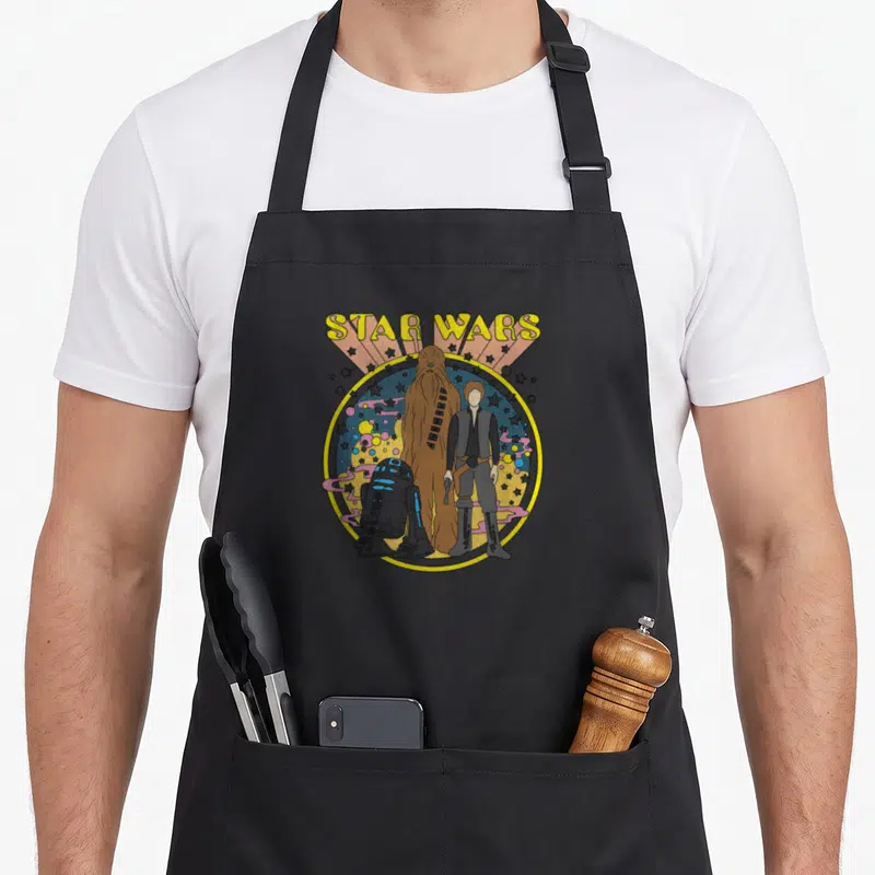 Tablier de cuisine noir avec illustration colorée de Luke Skywalker, Chewbacca et R2-D2 en style psychédélétique vintage.
