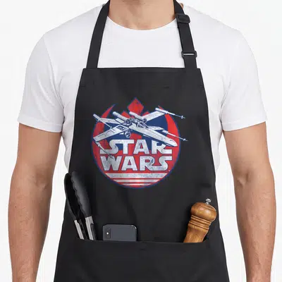 Tablier de cuisine noir avec illustration vintage d'un chasseur X-wing sur fond circulaire rouge et bleu.