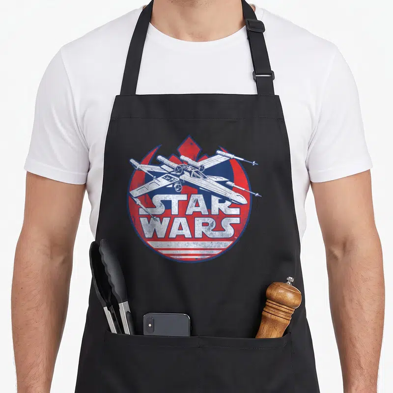 Tablier de cuisine noir avec illustration vintage d'un chasseur X-wing sur fond circulaire rouge et bleu.