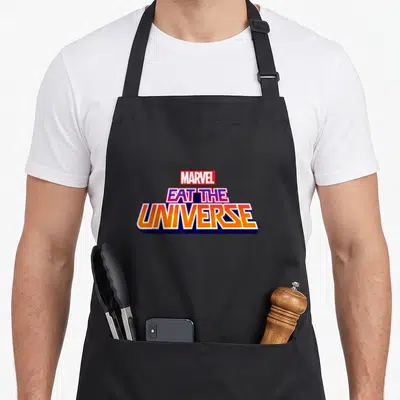 Tablier de cuisine noir avec le logo Marvel Eat the Universe aux couleurs vives et style rétro.