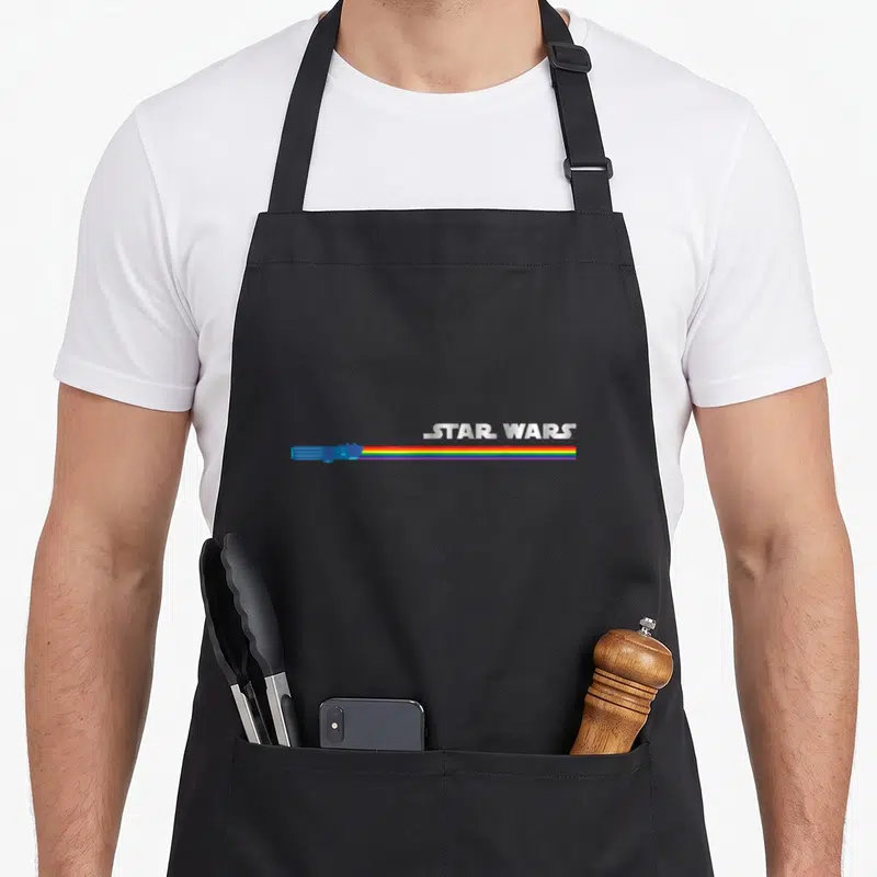 Tablier de cuisine noir avec sabre laser arc-en-ciel et logo Star Wars argenté sur le devant.