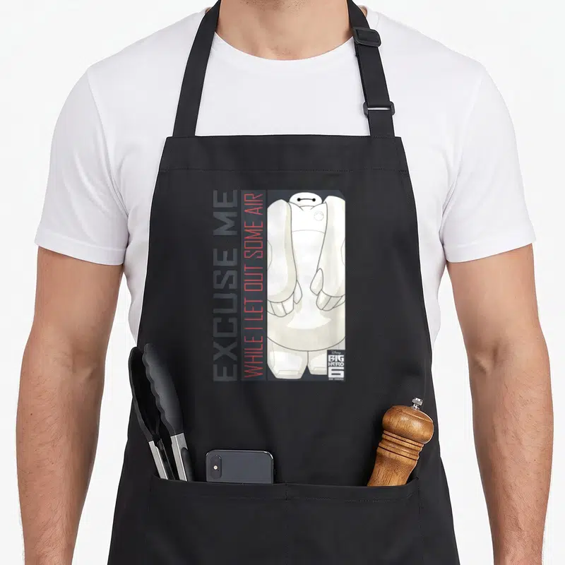 Tablier de cuisine noir avec illustration de Baymax et texte vertical Excuse Me While I Let Out Some Air en gris et rouge.