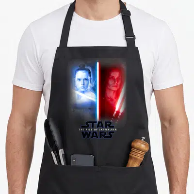 Tablier de cuisine noir avec Rey et Kylo Ren divisés par un sabre laser bleu et rouge.