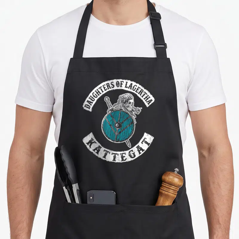 Tablier de cuisine noir avec illustration bouclier viking turquoise et inscription Daughters of Lagertha Kattegat en blanc.