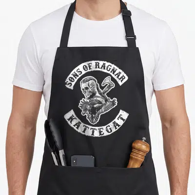 Tablier de cuisine noir avec illustration blanche d'un crâne viking coiffé d'une hache et d'un corbeau, encadré par le texte Sons of Ragnar Kattegat.