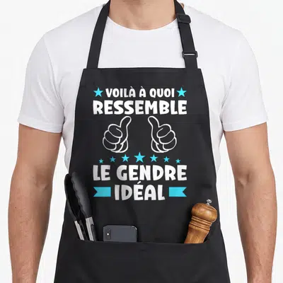 Tablier de cuisine noir avec inscription blanche et bleue « Voilà à quoi ressemble le gendre idéal » surmonté de deux pouces levés stylisés.
