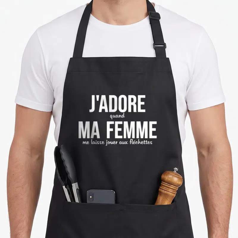 Tablier de cuisine noir avec le texte blanc J'adore quand ma femme me laisse jouer aux fléchettes imprimé au centre du torse.