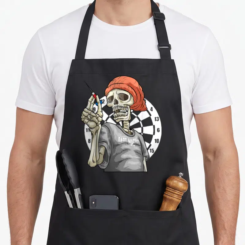 Tablier de cuisine noir avec un squelette portant un bonnet orange et tenant une fléchette devant une cible de darts.
