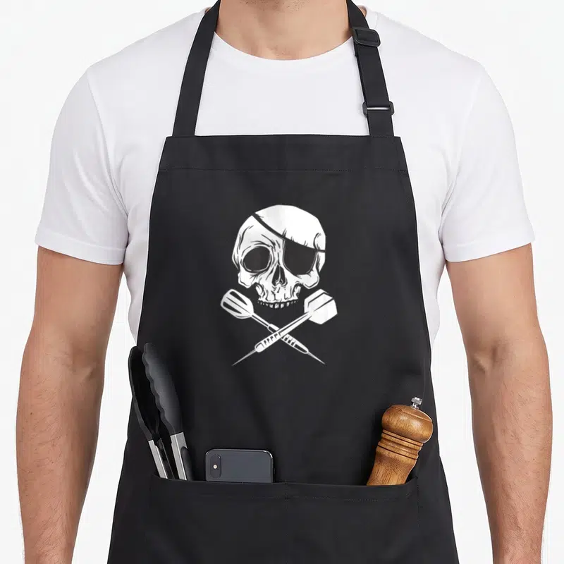 Tablier de cuisine noir avec un crâne de pirate et deux fléchettes croisées en dessin blanc.