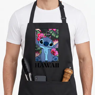 Tablier de cuisine noir avec illustration de Stitch entouré de fleurs d'hibiscus et du mot Hawaii.