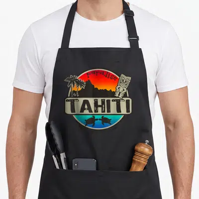Tablier de cuisine noir avec logo tahitien montrant un soleil, des palmiers, une statue tiki et deux tortues marines.