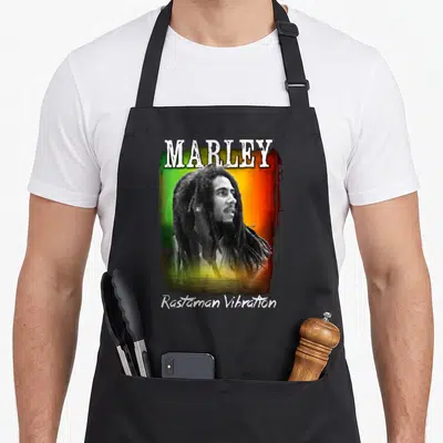 Tablier de cuisine noir avec portrait de Bob Marley sur fond vert jaune rouge et texte Marley Rastaman Vibration