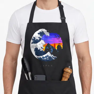 Tablier de cuisine noir avec une grande vague bleue, des montagnes et un temple torii rouge sur fond de coucher de soleil violet et orange.