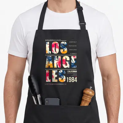 Tablier de cuisine noir avec typographie Los Angeles remplie de palmes roses et bleues ainsi que les mots California 1984.