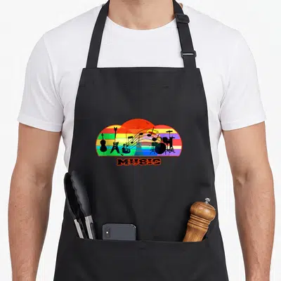 Tablier de cuisine noir avec illustration colorée d'instruments de musique sur fond arc-en-ciel et le mot MUSIC imprimé en dessous.