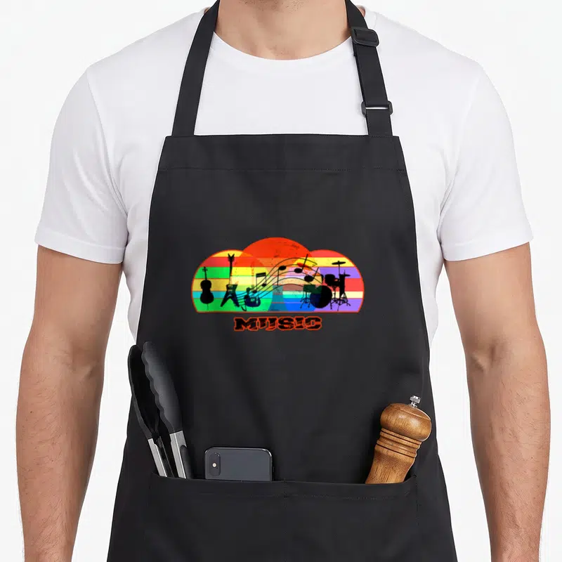Tablier de cuisine noir avec illustration colorée d'instruments de musique sur fond arc-en-ciel et le mot MUSIC imprimé en dessous.