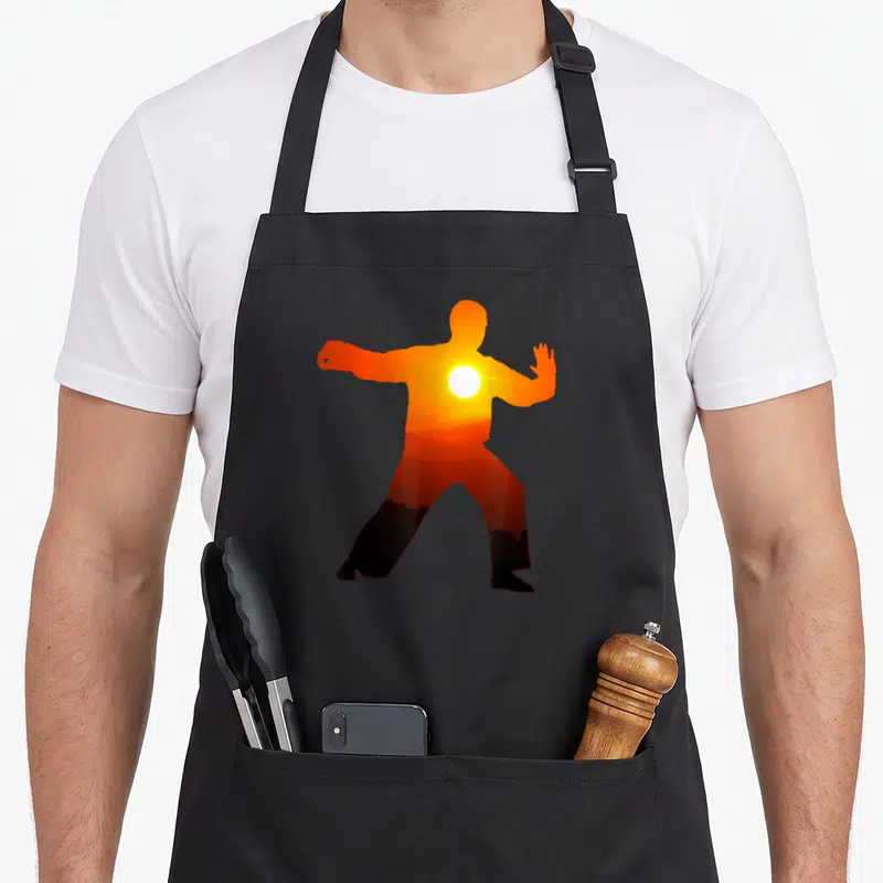 Tablier de cuisine noir avec silhouette orange effectuant un mouvement de Tai Chi et un soleil brillant au niveau du torse.