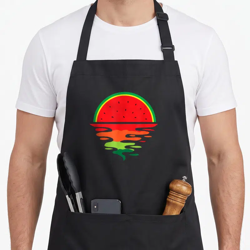 Tablier de cuisine noir avec illustration d'une pastèque formant un coucher de soleil aux couleurs vives et son reflet ondulé.