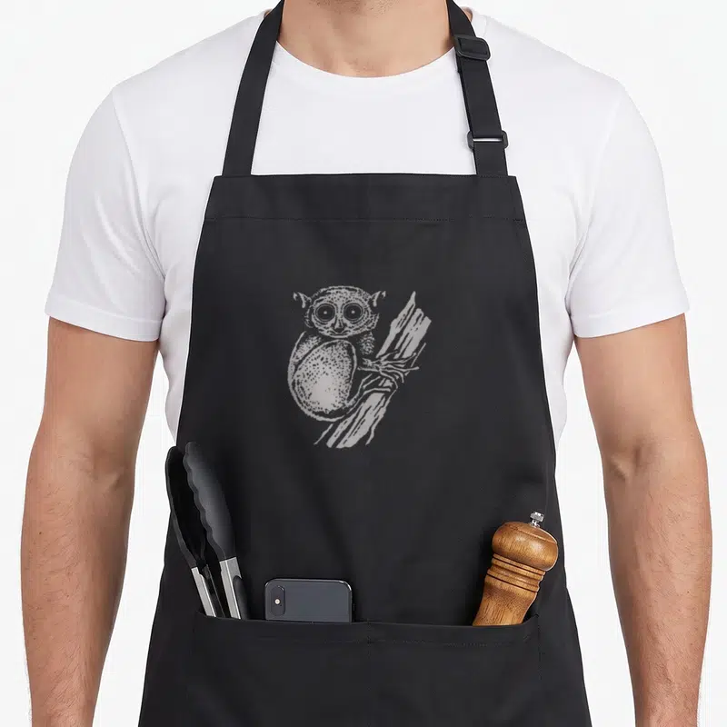 Tablier de cuisine noir avec illustration d'un tarsier aux grands yeux accroché à une branche d'arbre.