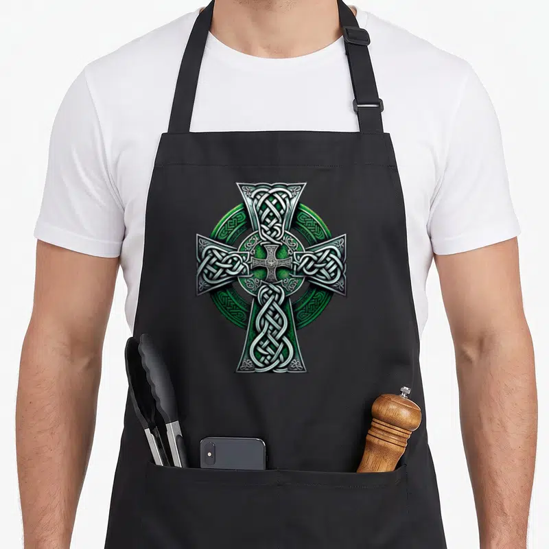 Tablier de cuisine noir avec une grande croix celtique verte et argentée au centre du torse.
