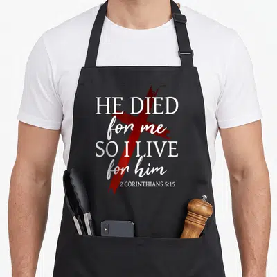 Tablier de cuisine noir avec une croix rouge et le texte He died for me so I live for him en blanc.