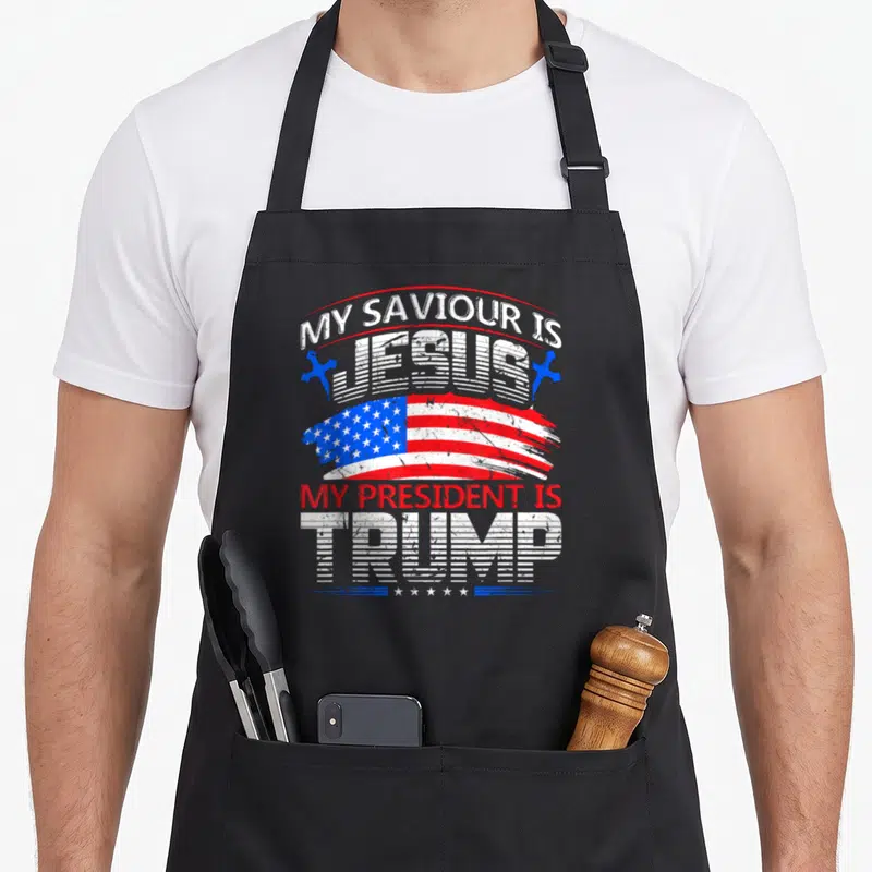 Tablier de cuisine noir avec typographie My Saviour Is Jesus My President Is Trump et drapeau américain stylisé.