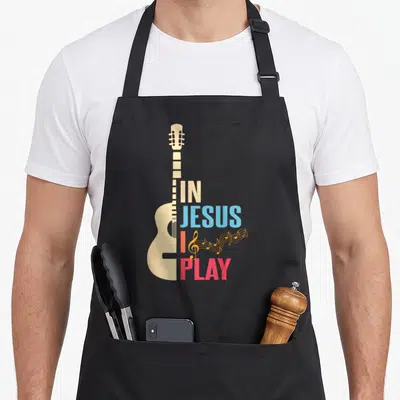 Tablier de cuisine noir avec illustration de guitare beige et texte multicolore En Jésus je joue.