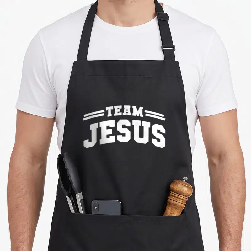 Tablier de cuisine noir avec l'inscription Team Jesus en lettres blanches style sportif et deux lignes décoratives au-dessus du texte.