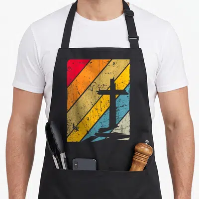 Tablier de cuisine noir avec une croix grise sur fond de bandes diagonales rouges oranges jaunes et bleues texturées.