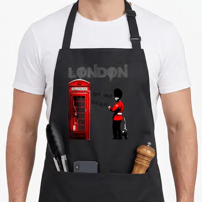 Tablier de cuisine noir avec un gardien royal, une cabine téléphonique rouge et le texte God save the Queen en graffiti.