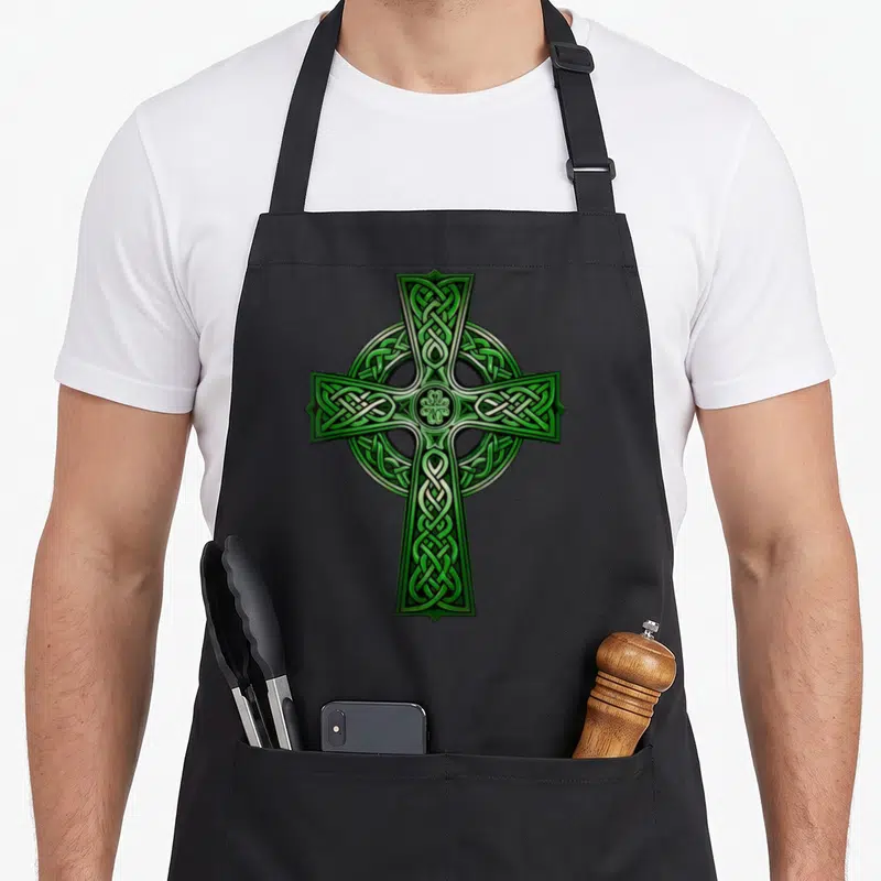 Tablier de cuisine noir avec une grande croix celtique verte à nœuds entrelacés et motif central trèfle.