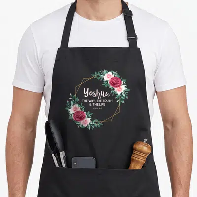 Tablier de cuisine noir avec une couronne de roses roses et un cadre géométrique doré.