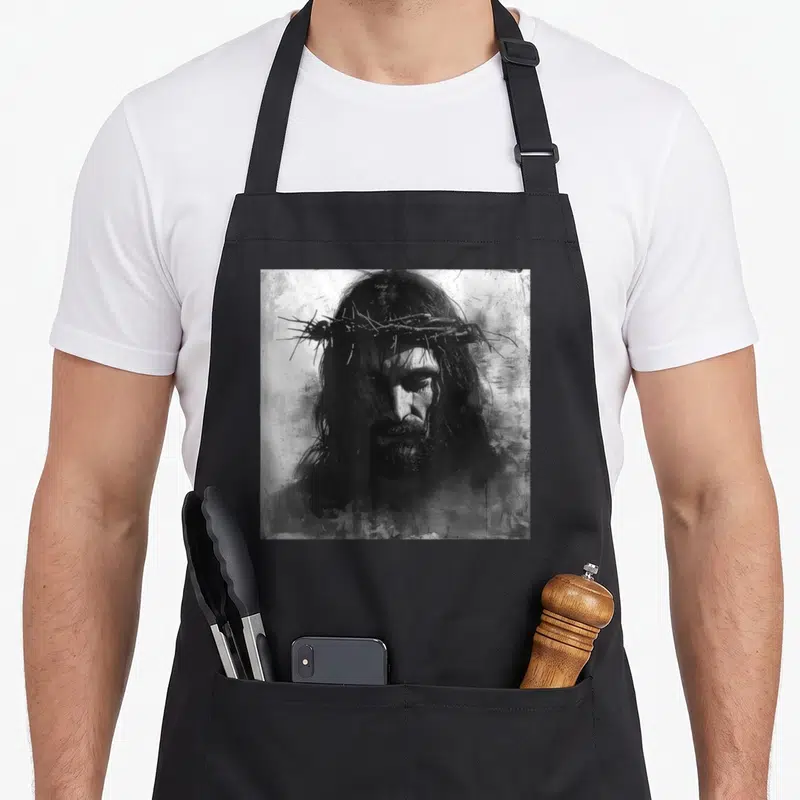 Tablier de cuisine noir avec illustration monochrome de Jésus Christ coiffé d'une couronne d'épines au style gravure expressive.