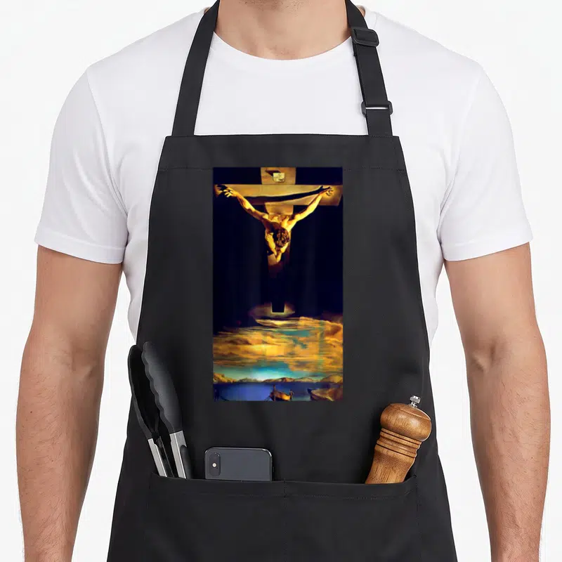 Tablier de cuisine noir avec une reproduction de la Crucifixion de Salvador Dali imprimée sur le devant.
