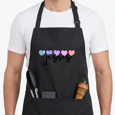 Tablier de cuisine noir avec le mot Jésus en noir sur cinq cœurs colorés pastel alignés.
